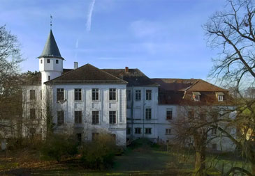 Herrschaftliches Schloss mit charakteristischem Turm und klassischer weißer Fassade, umgeben von parkähnlichem Grundstück.