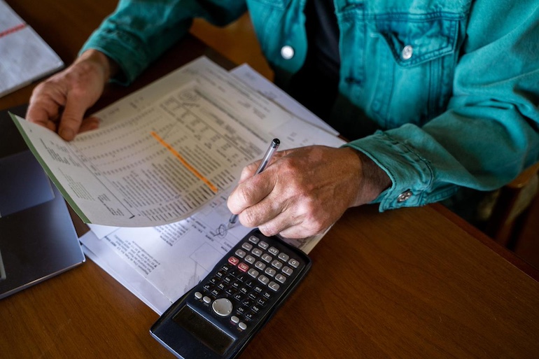 Person berechnet optimale Tilgung, Dokumente in der Hand, Taschenrechner auf dem Tisch