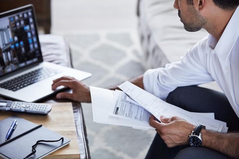 Makler hat alle Formulare für den Verkauf in der Hand und sitzt am Laptop