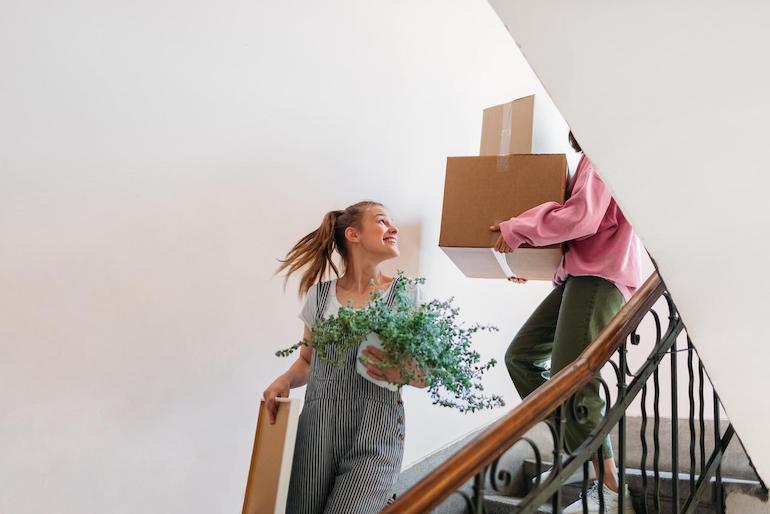 Freunde tragen Kartons und Pflanzen zum beendeten Mietverhältnis die Treppe runter